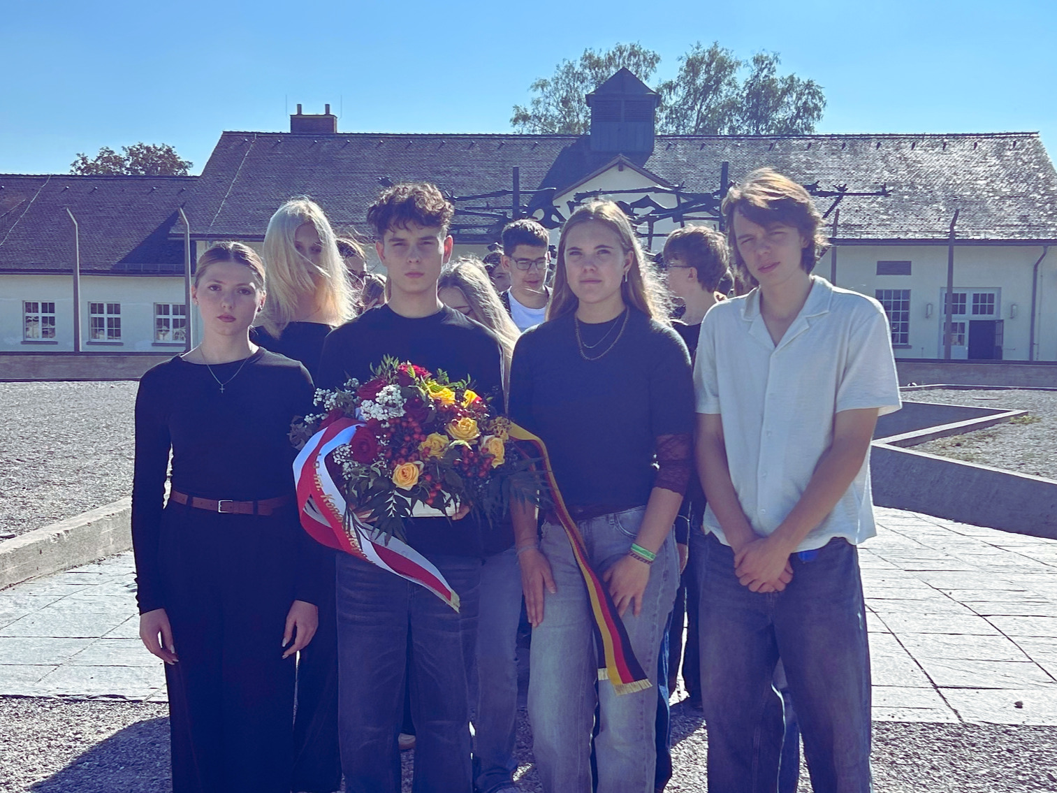 Gruppe von Schülern mit Blumengebinde vor dem Mahnmal in der Gedenkstätte Dachau